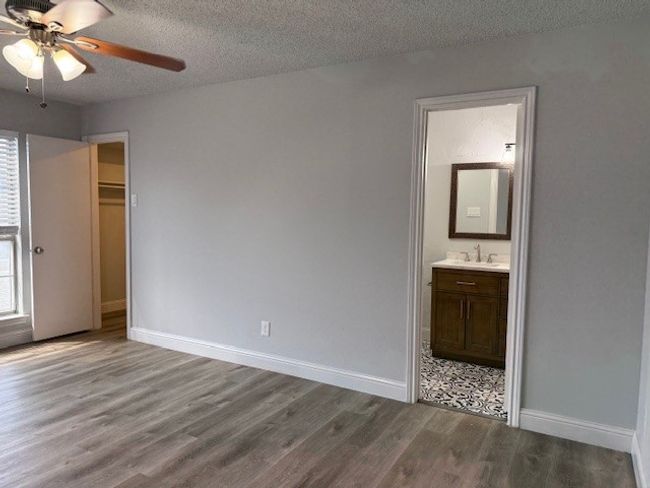 Unfurnished bedroom with wood finished floors, a textured ceiling, multiple windows, ensuite bath, and a ceiling fan | Image 6