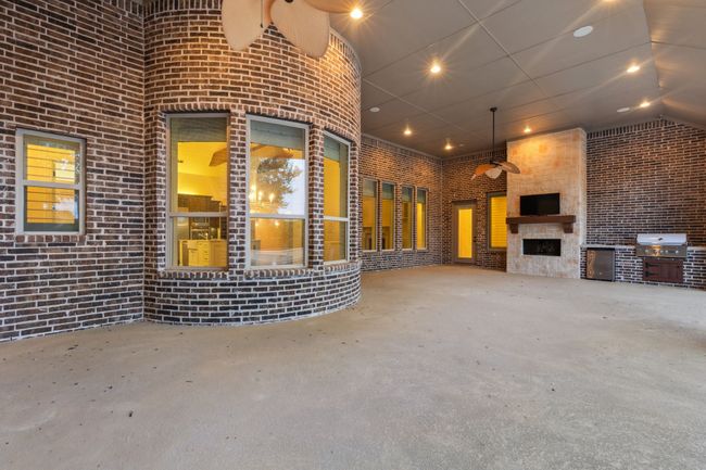 Double triple oversized patio for outdoor gathering featuring stainless steel grill, beverage fridge, TV over a stony fireplace, concrete flooring, and recessed lighting | Image 36