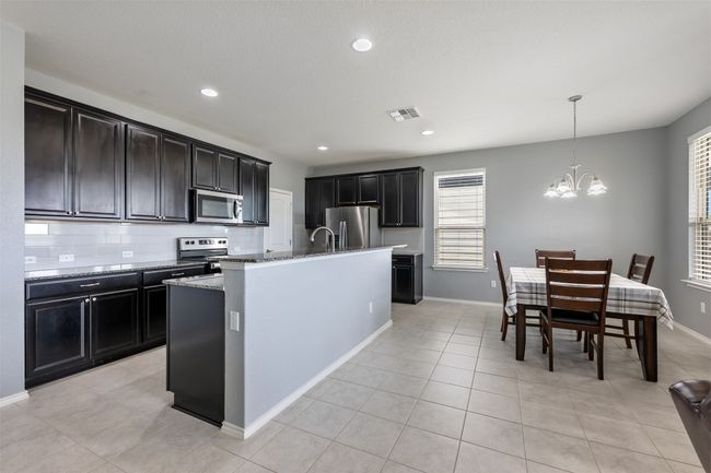 Kitchen featuring an inviting chandelier, visible vents, light stone countertops, a kitchen island with sink, and appliances with stainless steel finishes | Image 13