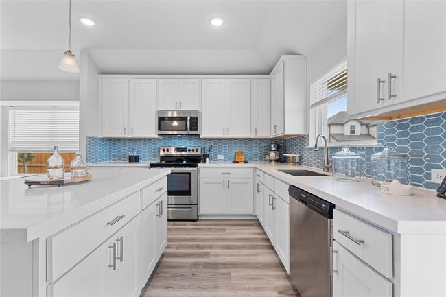 Kitchen with appliances with stainless steel finishes, a sink, light countertops, white cabinetry, and recessed lighting | Image 13