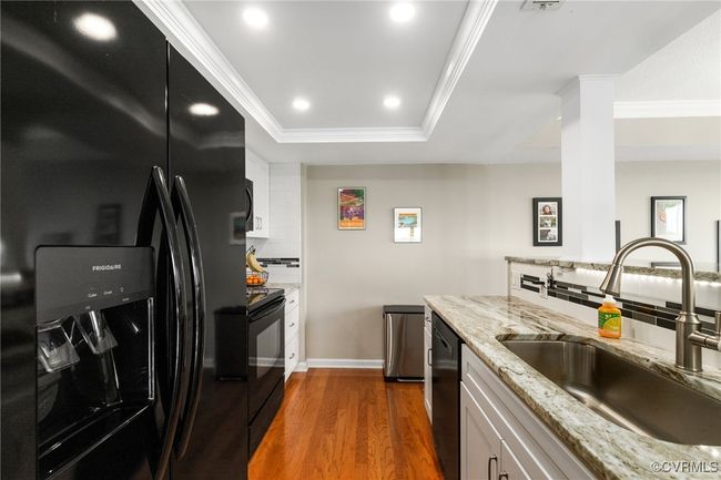 Kitchen with a sink, dark wood-style flooring, black appliances, white cabinetry, and ornamental molding | Image 11