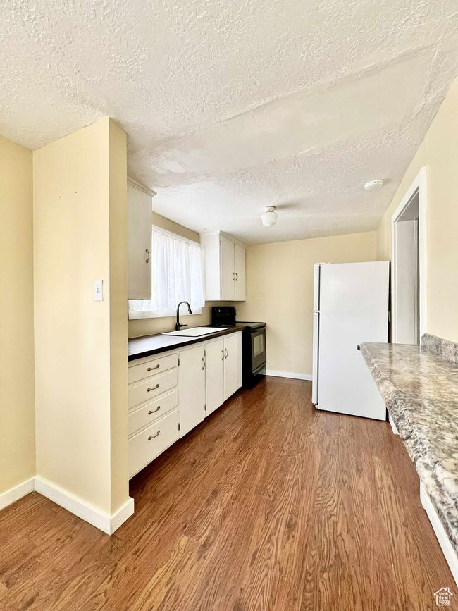 Kitchen featuring wood finished floors, freestanding refrigerator, black / electric stove, and a textured ceiling | Image 14