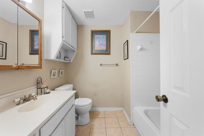 Bathroom featuring vanity, tile patterned flooring, a textured ceiling, toilet, and washtub / shower combination | Image 13