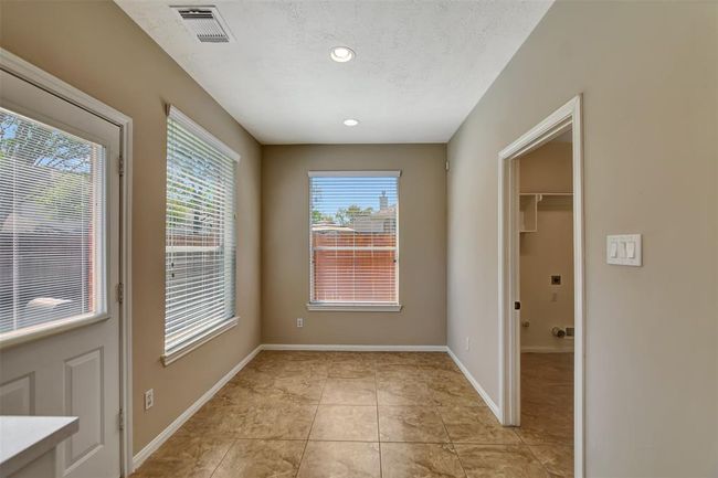 Bright utility room with tiled flooring, a door to the exterior, and two large windows providing ample natural light. Adjacent laundry area with hookups. | Image 25