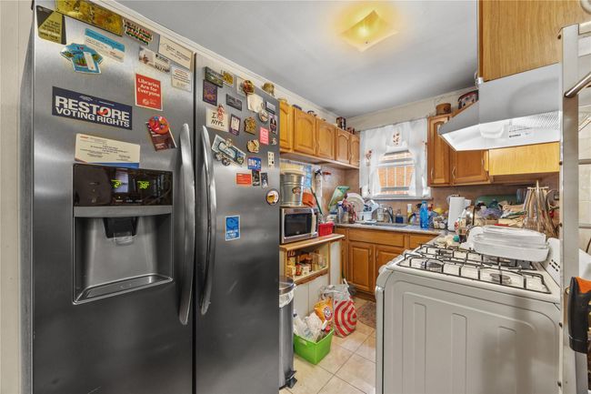 Kitchen with stainless steel appliances, light tile patterned floors, brown cabinets, and light countertops | Image 24