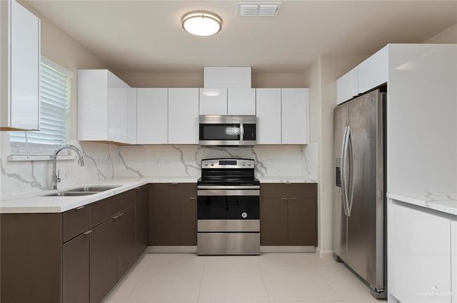Kitchen with appliances with stainless steel finishes, backsplash, white cabinets, and dark brown cabinetry | Image 4