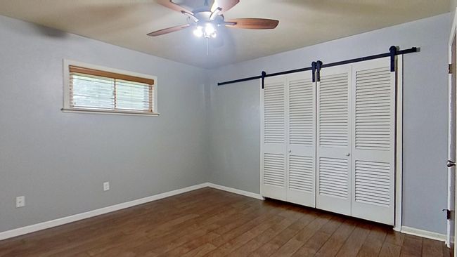 Unfurnished bedroom with a barn door, dark wood-type flooring, and baseboards | Image 14