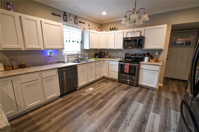 Kitchen featuring stainless steel appliances, a sink, ornamental molding, a chandelier, and light countertops | Image 11