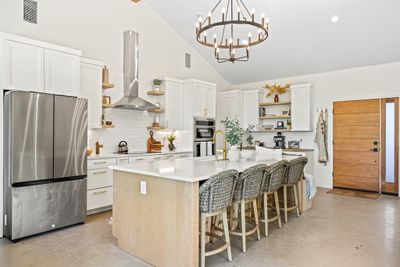 Kitchen with appliances with stainless steel finishes, white cabinets, island range hood, an inviting chandelier, and a kitchen island with sink | Image 2