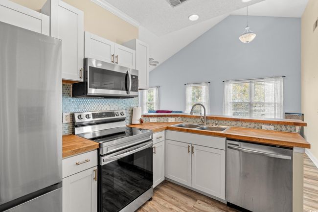 Kitchen with light wood-type flooring, stainless steel appliances, a sink, butcher block counters, and a peninsula | Image 8