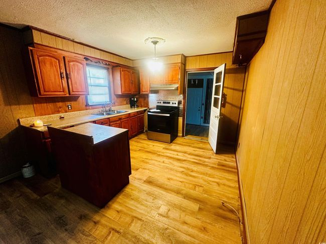 Kitchen featuring stainless steel electric range oven, under cabinet range hood, wood walls, light wood finished floors, and a sink | Image 9