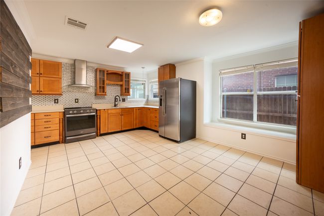 Kitchen with crown molding, wall chimney exhaust hood, stainless steel appliances, tasteful backsplash, and light tile patterned floors | Image 5