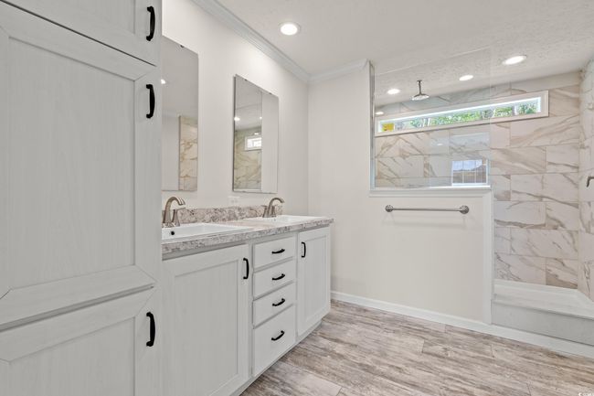 Bathroom featuring walk in shower, a sink, crown molding, double vanity, and wood finished floors | Image 18
