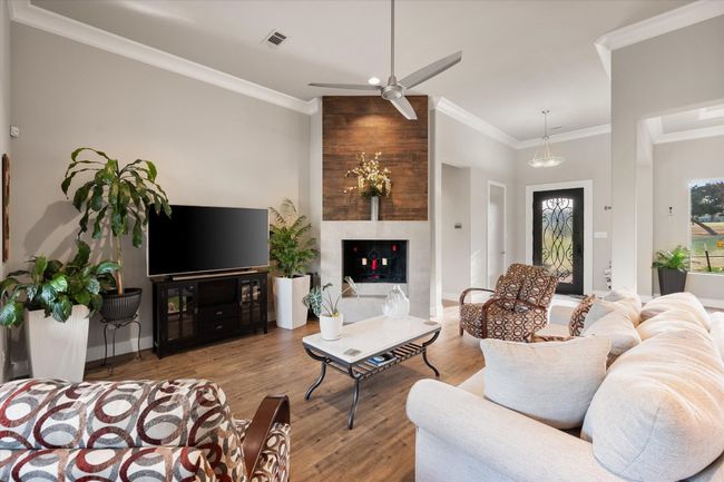 Living room with unique custom wood burning fireplace, ceiling fan, crown molding, and beautiful wood look tile floors | Image 4