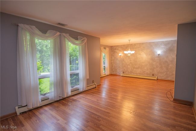 Spare room with baseboard heating, a chandelier, and wood finished floors | Image 6