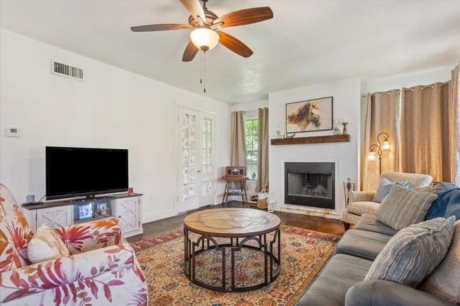 Living room with a fireplace, visible vents, ceiling fan, and wood finished floors | Image 6