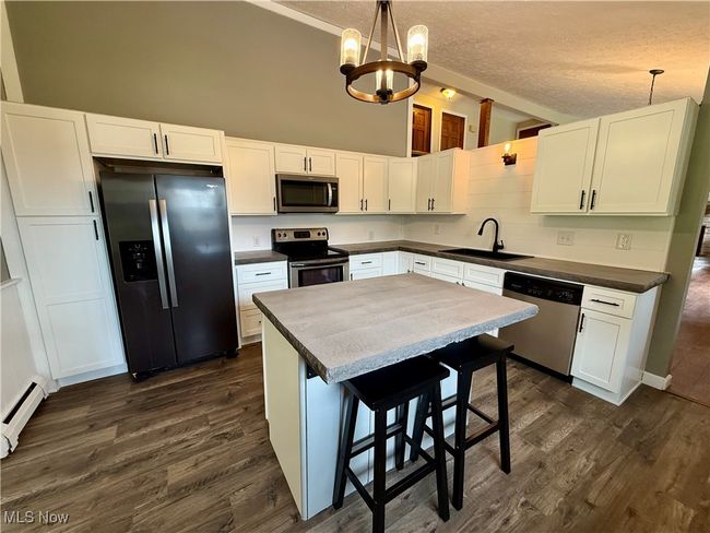 Kitchen featuring a chandelier, stainless steel appliances, white cabinets, a sink, and dark wood-type flooring | Image 15