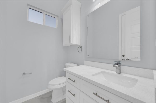 This bathroom features a modern design with a sleek white vanity, a large mirror, and chrome fixtures. There's a compact window for natural light, and the space is finished with light-colored walls and tile flooring for a clean, bright look. | Image 17