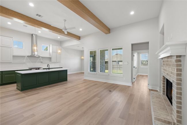 Kitchen featuring beam ceiling, hanging light fixtures, a brick fireplace, light hardwood / wood-style flooring, and range hood | Image 6