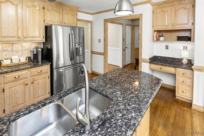 Kitchen featuring stainless steel fridge with ice dispenser, light brown cabinets, dark wood-style flooring, a wainscoted wall, and crown molding | Image 12