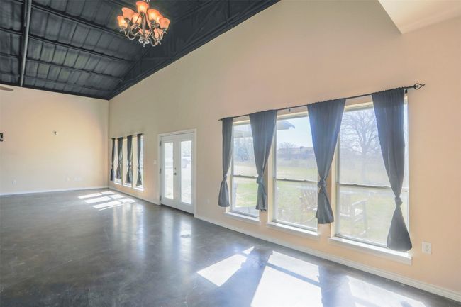Spare room with concrete flooring, high vaulted ceiling, baseboards, french doors, and an inviting chandelier | Image 11