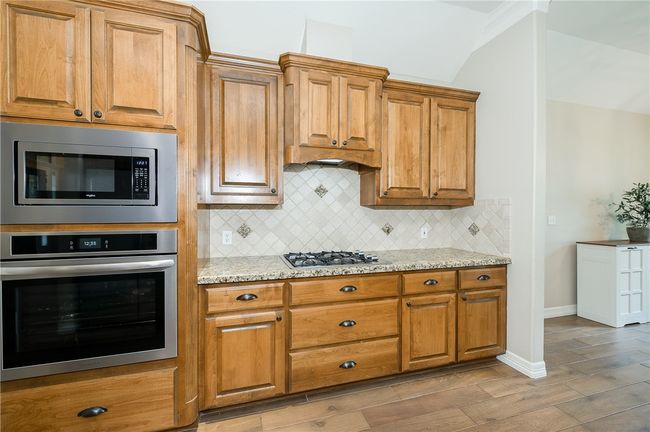Kitchen featuring light stone counters, decorative backsplash, stainless steel appliances, brown cabinets, and baseboards | Image 10