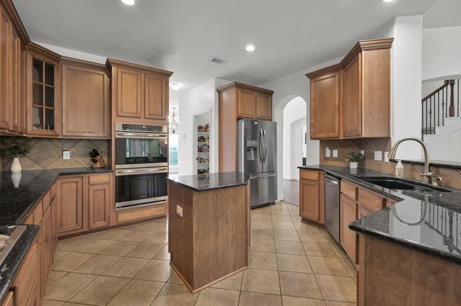 The large and roomy kitchen offers abundant granite countertop space that pairs beautifully with the natural wood finish cabinetry. These are not your builder basic cabinets. The ribbon design on the crown molding at the top of the cabinets gives an elegant and finished appearance. | Image 14