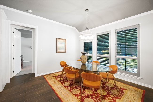 Dining area with baseboards, dark wood-style flooring, crown molding, a chandelier, and vaulted ceiling | Image 12