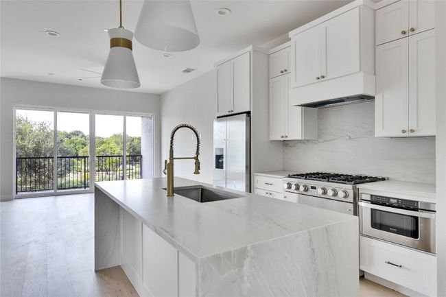 Kitchen with a sink, stainless steel appliances, an island with sink, backsplash, and custom range hood | Image 24