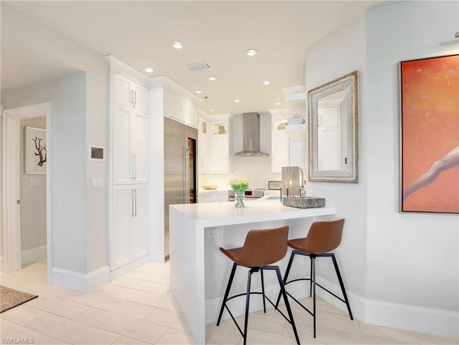 Kitchen with wall chimney exhaust hood, a breakfast bar area, a peninsula, white cabinets, and light countertops | Image 13