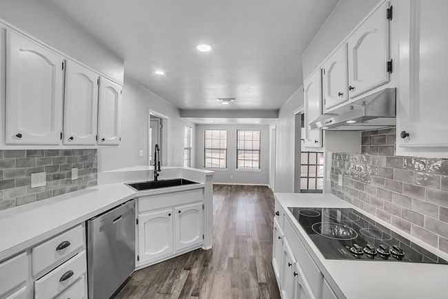 Kitchen featuring a peninsula, a sink, under cabinet range hood, dishwasher, and black electric stovetop | Image 5