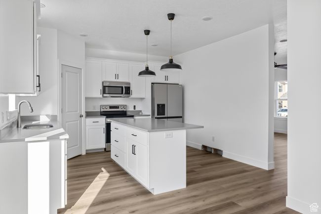 Kitchen with white cabinets, a sink, appliances with stainless steel finishes, a center island, and light wood-type flooring | Image 5