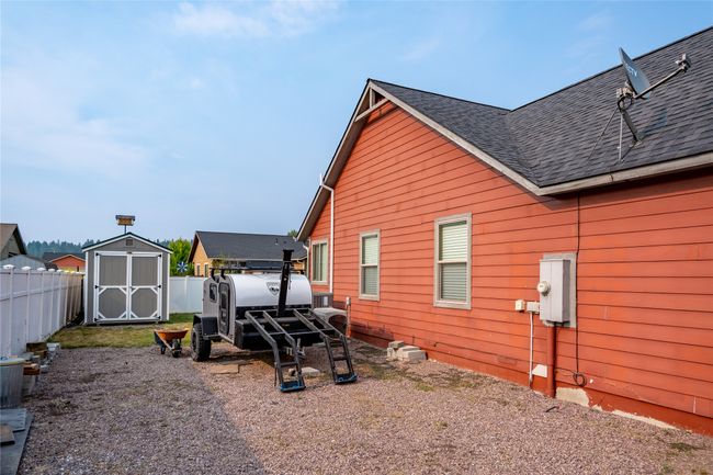 View of side of home featuring a shingled roof, a storage unit, fence, and an outbuilding | Image 18