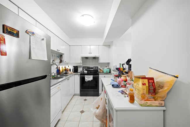 Kitchen with white dishwasher, light tile patterned flooring, black / electric stove, white cabinetry, and freestanding refrigerator | Image 4