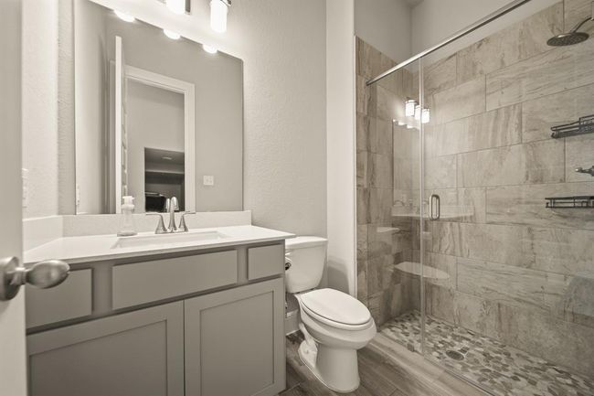 Modern bathroom with walk-in shower, stone flooring, quartz vanity, and sleek tile surround. | Image 22