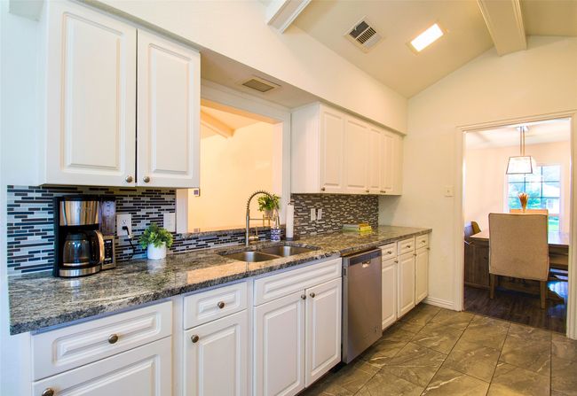 Kitchen featuring white cabinetry, stainless steel dishwasher, backsplash, dark marble finish floors, and dark stone countertops | Image 12