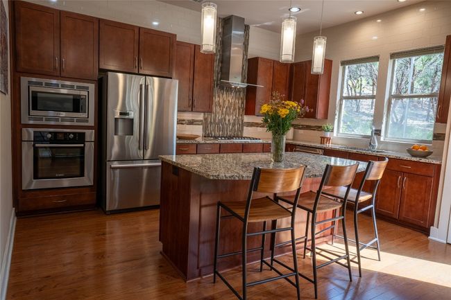 Kitchen with appliances with stainless steel finishes, wall chimney exhaust hood, dark wood finished floors, tasteful backsplash, and a kitchen island | Image 9