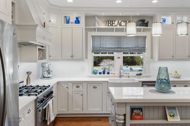 Kitchen featuring light countertops, a sink, open shelves, appliances with stainless steel finishes, and custom range hood | Image 10
