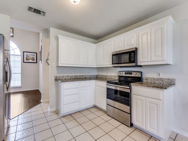 Kitchen with stainless steel appliances, white cabinetry, baseboards, light tile patterned flooring, and dark stone countertops | Image 13