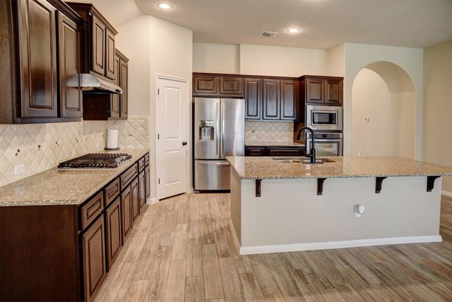 Kitchen with appliances with stainless steel finishes, a kitchen breakfast bar, light wood-style floors, dark brown cabinetry, and recessed lighting | Image 13