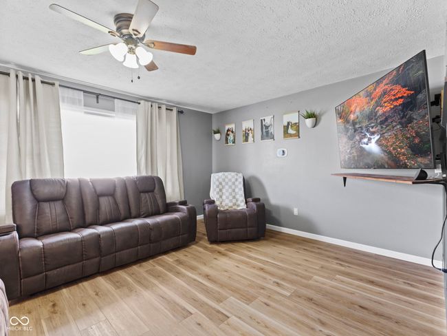 living area with a textured ceiling, ceiling fan, baseboards, and light wood-style floors | Image 7
