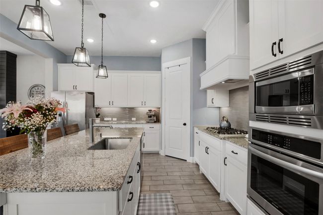 Kitchen with appliances with stainless steel finishes, a sink, tasteful backsplash, an island with sink, and white cabinets | Image 10