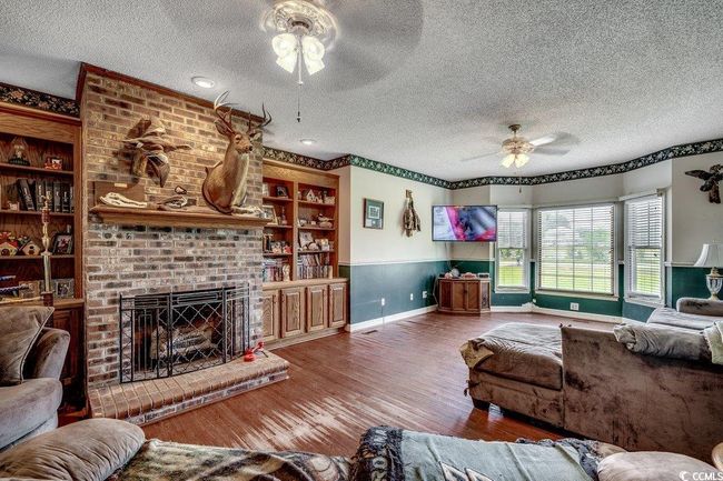 Living room with ceiling fan, a textured ceiling, baseboards, and wood finished floors | Image 8