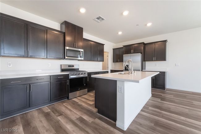 Kitchen featuring appliances with stainless steel finishes, light countertops, dark wood-type flooring, a center island with sink, and recessed lighting | Image 11
