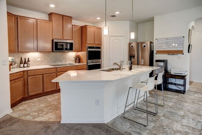 Kitchen with stainless steel appliances, a kitchen island with sink, light countertops, decorative light fixtures, and tasteful backsplash | Image 5