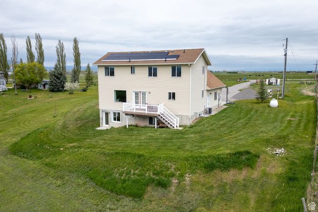 Back of house featuring solar panels, a deck, stairway, a yard, and a shingled roof | Image 26