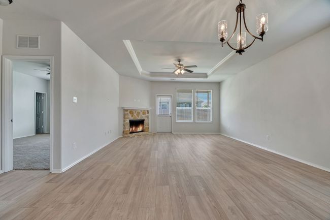 Unfurnished living room featuring ceiling fan, a raised ceiling, light wood finished floors, and a fireplace | Image 13