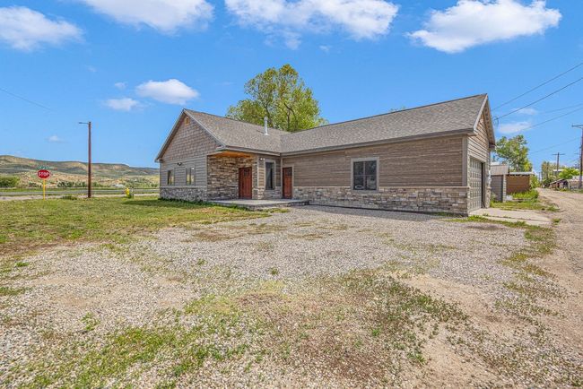 View of front facade with stone siding, a shingled roof, an attached garage, and driveway | Image 8