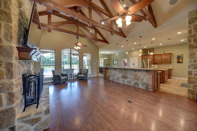 Experience the warmth of this inviting living room, featuring an elegant stone fireplace, expansive windows with serene views, and impressive exposed beam ceilings. Perfect for relaxation and entertaining. | Image 6