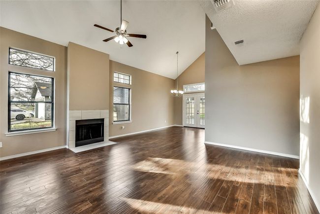Unfurnished living room with a ceiling fan, a tiled fireplace, dark wood-type flooring, high vaulted ceiling, and a chandelier | Image 4